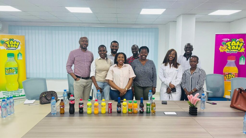 Das africon-Team und Mitarbeitende von Bakhresa Food Products vor Tam-Tam-Markendisplays während des Fabrikbesuchs in Daressalam