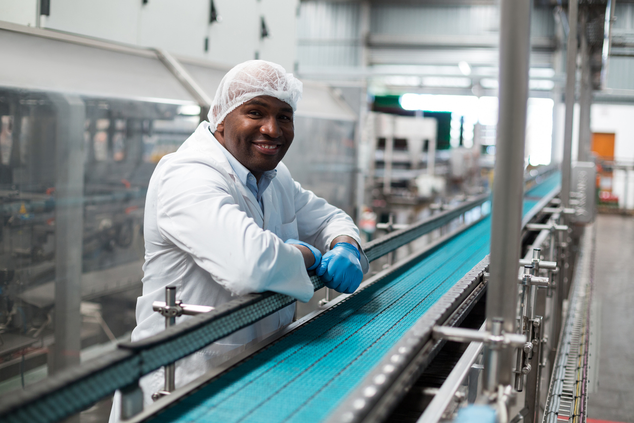 Portrait of factory engineer leaning on production line in drinks production plant